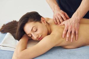 Young woman is lying down when man doing massage of her back at spa photo