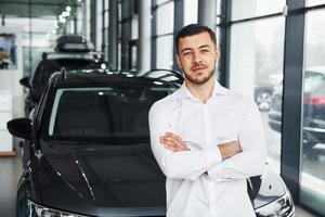 Young man in white shirt is indoors with modern new automobile photo