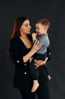 Mother in stylish black clothes is with her little son in the studio photo