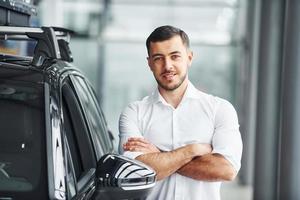 un joven con camisa blanca está adentro con un automóvil nuevo y moderno foto