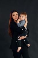 madre con ropa negra elegante está con su pequeño hijo en el estudio foto