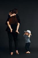 Woman in black stylish clothes is with her little son and daughter in the studio photo