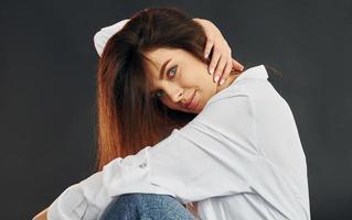 In white shirt and blue jeans. Young beautiful woman is posing for the camera in the studio photo