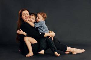 Woman in black stylish clothes is with her little son and daughter in the studio photo