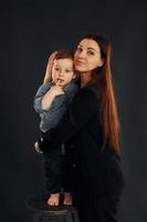 Mother in stylish black clothes is with her little son in the studio photo