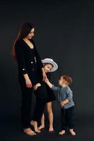 Woman in black stylish clothes is with her little son and daughter in the studio photo