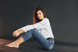 se sienta en el suelo. joven hermosa mujer está posando para la cámara en el estudio foto