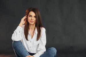 In white shirt and blue jeans. Young beautiful woman is posing for the camera in the studio photo