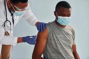 Professional young african american doctor giving injection to patient in hospital photo