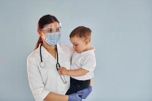 Young nurse in white coat and with stethoscope holds little boy in hands photo