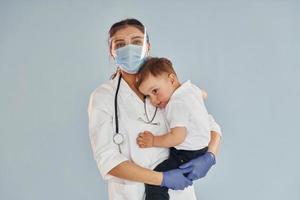 Young nurse in white coat and with stethoscope holds little boy in hands photo