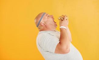 With fast food. Funny overweight man in sportive head tie is against yellow background photo