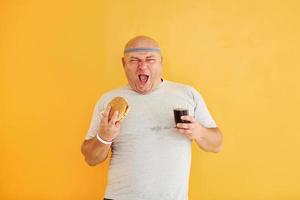 With fast food. Funny overweight man in sportive head tie is against yellow background photo