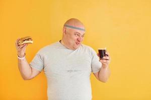 With fast food. Funny overweight man in sportive head tie is against yellow background photo
