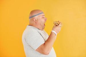 With fast food. Funny overweight man in sportive head tie is against yellow background photo