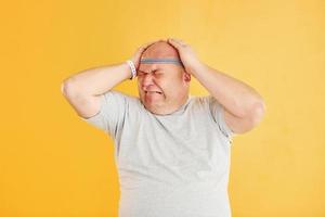 Funny overweight man in sportive head tie is against yellow background photo