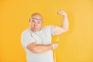 Funny overweight man in sportive head tie is against yellow background photo