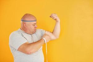 Funny overweight man in sportive head tie is against yellow background photo