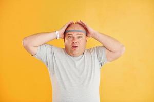 Funny overweight man in sportive head tie is against yellow background photo