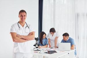 Man standing and posing. Group of young doctors is working together in the modern office photo