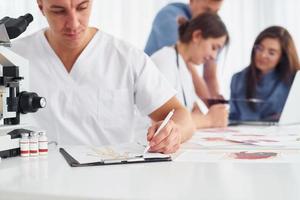 Man with microscope. Group of young doctors is working together in the modern office photo