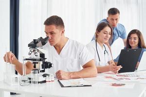 Man with microscope. Group of young doctors is working together in the modern office photo
