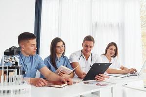 Sitting by the table. Group of young doctors is working together in the modern office photo