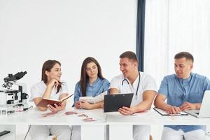 Sitting by the table. Group of young doctors is working together in the modern office photo