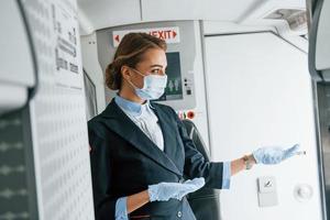 en guantes protectores y máscara. joven azafata en el trabajo en el avión de pasajeros foto