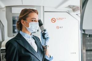 Uses phone. Young stewardess on the work in the passanger airplane photo