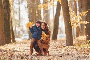 vista frontal. madre con su hijo se divierte al aire libre en el bosque de otoño foto