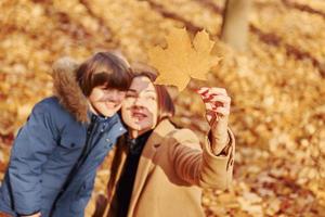 Looking at leaf. Mother with her son is having fun outdoors in the autumn forest photo