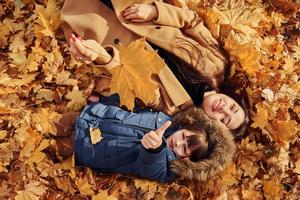 acostándose sobre las hojas. madre con su hijo se divierte al aire libre en el bosque de otoño foto