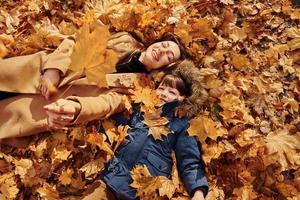 acostándose sobre las hojas. madre con su hijo se divierte al aire libre en el bosque de otoño foto