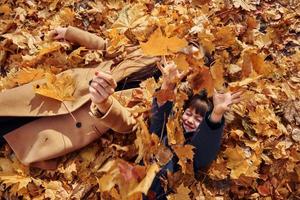 acostándose sobre las hojas. madre con su hijo se divierte al aire libre en el bosque de otoño foto