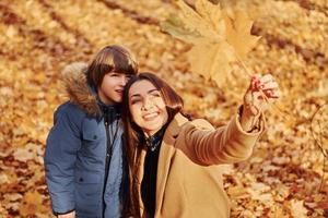 Looking at leaf. Mother with her son is having fun outdoors in the autumn forest photo