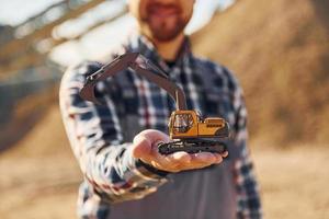 Holding toy. Construction worker in uniform is on the quarry photo