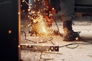 Sparks flying. Close up view of man's legs and hands with slicing tool. Working with metal