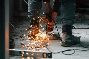 Sparks flying. Close up view of man's legs and hands with slicing tool. Working with metal photo