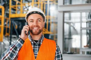Talking by phone. Construction worker in uniform is in the factory photo