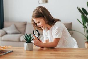 Little girl is sitting by the table with magnifying glass photo