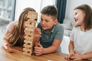 Focused on the jumbling tower game. Kids having fun in the domestic room at daytime together photo