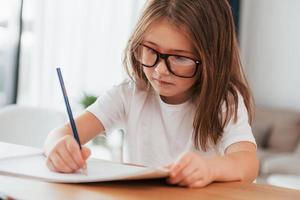 la niña está sentada junto a la mesa y está aprendiendo a dibujar foto