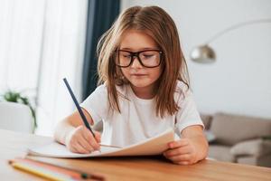 la niña está sentada junto a la mesa y está aprendiendo a dibujar foto