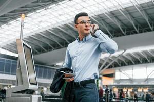 Holding phone. Young businessman in formal clothes is in the airport at daytime photo