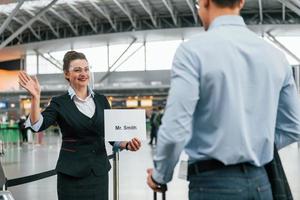 Meet by the woman with text. Young businessman in formal clothes is in the airport at daytime photo