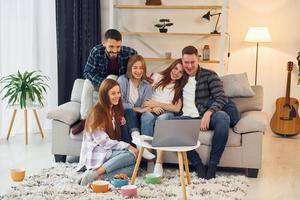 usando una computadora portátil grupo de amigos hacen fiesta juntos en el interior foto