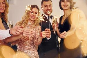 With sparklers in hands. Group of people have a new year party indoors together photo