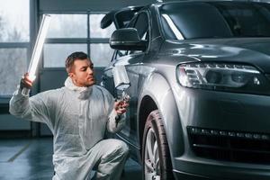 Illuminating the car surface. Man in uniform is working in the auto service photo