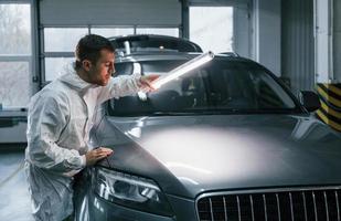 Illuminating the car surface. Man in uniform is working in the auto service photo